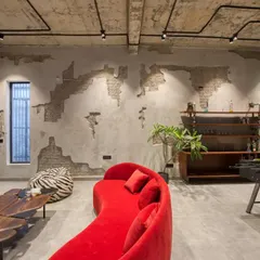 This industrial-style lounge area features exposed brick and concrete walls, a bright red curved sofa, and a foosball table, creating a fun and edgy entertainment space.