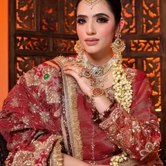 A detailed portrait of a model in a rich red bridal outfit. The shot emphasizes the heavy earrings, maang tikka, and the intricate handiwork on the dupatta.