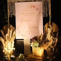 A personalized welcome sign for a boho-chic cocktail party. This setup combines elegant calligraphy with natural elements like pampas grass, dried palms, and a macrame frame to set a warm and stylish tone right from the entrance.