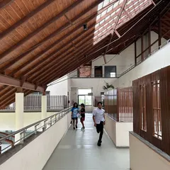 Students running along a wide, airy corridor at Vellore International School. The wooden-clad sloping roof and open design create a warm and dynamic space that encourages movement and play.