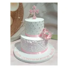 A beautiful two-tiered confirmation cake with a unique offset design. It features intricate lace work and a delicate pink cross and flower.