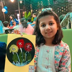 A happy guest proudly holding up the floral artwork she created using bubble wrap and leaf impression techniques. Each child gets to explore different textures and methods.