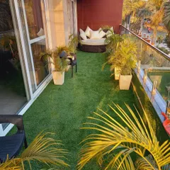 For this spacious Gurgaon balcony, I used wall-to-wall artificial grass to create a lawn-like feel. The space is furnished with a large, comfortable daybed and surrounded by potted palms, making it an ideal outdoor lounge area.