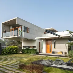 A frontal view of The Quarry House, showcasing the interplay of cantilevered masses. The upper volume provides shade and drama, while the ground floor remains open and connected to the landscape, featuring a tranquil water feature with quarry stones.