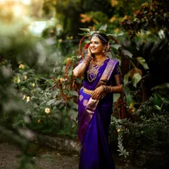 A stunning bridal portrait of the bride in her deep purple Kanjeevaram saree, set against a lush green backdrop. I used natural light to highlight the intricate gold jewelry and the joyful expression on her face.
