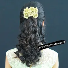 A romantic half-up hairstyle with soft curls at the ends. The look is finished with a cluster of delicate cream-colored roses, making it perfect for a reception or party.