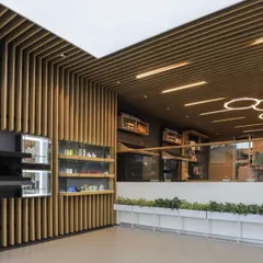 The reception and product display area at the Oriflame office, featuring modern circular light fixtures and vertical wood slats. The design is clean, bright, and reflects the brand's natural wellness identity.