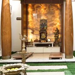 A close-up of the pooja area, showing the beautiful grain of the traditional wooden pillars and the warm, ambient light from the backlit onyx marble.