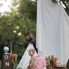 A little girl in a lovely pink dress explores her first birthday setup in a park. This candid shot captures her curiosity and movement, with a teepee and "ONE" blocks creating a magical, rustic scene.