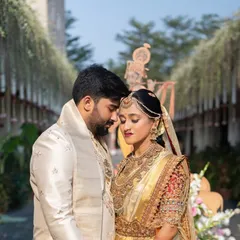 A close up of a groom and bride, showing the coordination in their outfits. His off white silk sherwani features subtle embroidery that echoes the craftsmanship of her golden bridal saree.