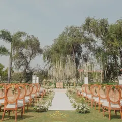 The view down the aisle, lined with elegant chairs and white floral arrangements, leading to a stunning mandap area under the trees. This is outdoor elegance at its finest.
