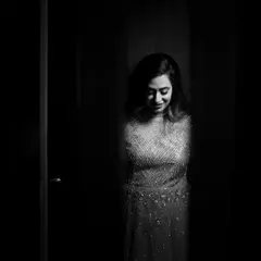 A mysterious and alluring black and white portrait of a bride peeking through a gap. The shadows create a sense of anticipation while highlighting her gentle smile.