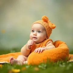 A professionally shot portrait of a baby in a cute orange outfit, sitting outdoors on a soft blanket. This highlights our outdoor baby photography service.