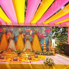 A closer look at the Haldi stage, featuring triangular structures covered in marigold and tuberose flowers against a tropical leaf and toucan print backdrop.