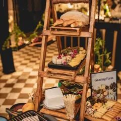 A "Grazing Farm" setup featuring a rustic ladder display for breads and cheeses. This innovative presentation style turns a simple food station into a decorative and memorable feature of the event.