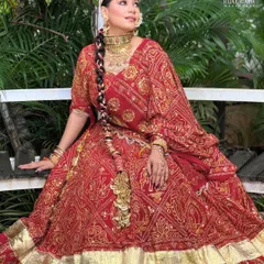 A full-length view of a stunning Marwadi bride in her traditional red bandhani lehenga. The makeup is kept classic and radiant to balance the grandeur of the outfit and heavy jewelry.