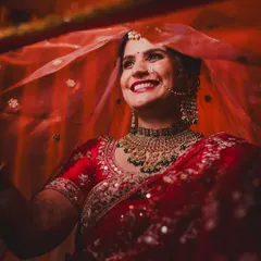 The joy of a North Indian bride is absolutely infectious. This candid shot captures her genuine happiness, with the vibrant red of her veil creating a classic and timeless bridal portrait that radiates warmth and excitement.