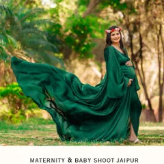 The wind catches the train of a beautiful green maternity gown in this dynamic outdoor shot. The mother-to-be, wearing a floral crown, looks serene and powerful in the natural setting.