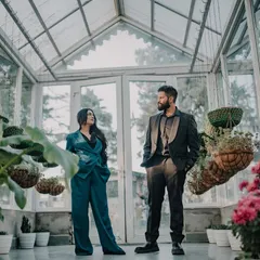 A stylish, full-length portrait of the couple in a modern glasshouse. The composition emphasizes their fashion-forward look against the unique architecture, perfect for a chic mountain pre-wedding shoot.