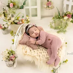 Sweet dreams on a tiny bed. This newborn is dressed in a cozy pink outfit, sleeping on a miniature bed adorned with beautiful flowers.
