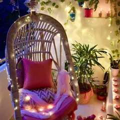 This design idea transforms a small balcony into a magical evening retreat with a comfortable swing chair, fairy lights, and climbing ivy, perfect for unwinding after a long day.