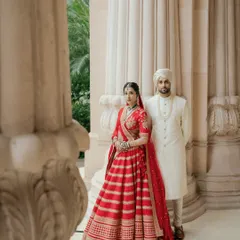 A classic portrait of Avin and Nikki at The Leela Palace, Bangalore. Their coordinated red and white outfits stand out beautifully against the palace's stately pillars.