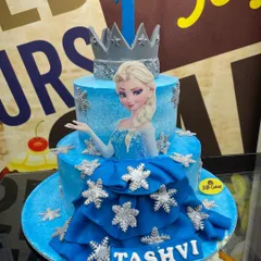 Let it go with this magical 4kg Frozen theme cake. This two-tiered creation features a fondant dress drape, an edible Elsa image, and sparkling snowflake details, perfect for a princess's party.