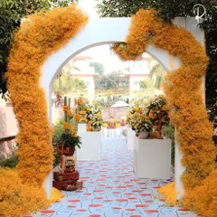 The entrance to the Haldi ceremony, featuring a white arch wrapped in fluffy, yellow-orange florals, leading onto a custom-printed poppy-patterned carpet.