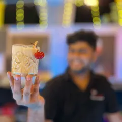 A beautifully crafted cocktail, held up by our bartender. The focus is on the drink itself: the crystal-clear ice, the perfect dilution, and the simple yet elegant cherry garnish.