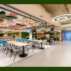 A wide shot of a corporate cafeteria we "green-ed up." The space features a mix of plant solutions, including planters, a green wall, and hanging greenery from the light fixtures, all working together to create a refreshing and inspiring place to eat and socialize.
