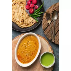 A rustic, top-down view of Dal Makhani with parathas and green chutney. The use of wooden textures and dark surfaces gives this shot a traditional and earthy feel.