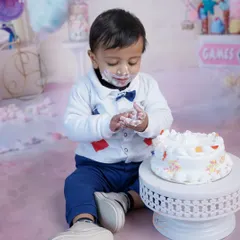 A full view of the cake smash scene, with the little one happily digging into his cake on a soft pink floor drop.