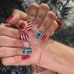A cozy and festive Christmas manicure. This design features a mix of patterns, including red and white stripes, green plaid, and red glitter, just like a Christmas sweater.