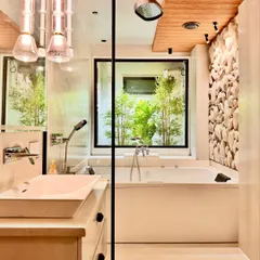 A different angle of the nature-inspired bathroom, highlighting the clean lines of the vanity and the modern chrome fixtures. The combination of the smooth bathtub, the textured stone wall, and the warm wood ceiling creates a balanced and serene environment.
