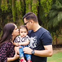 A tender family moment captured outdoors, with parents kissing their baby's cheeks.