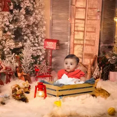 A cozy Christmas-themed studio shoot. The setup includes a snowy backdrop, festive trees, and warm lights to create a magical holiday portrait.