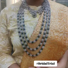 A client trying on a Victorian-style necklace with emerald green stones during her bridal trial. This process helps ensure the jewellery perfectly complements the outfit and the bride's personal style.
