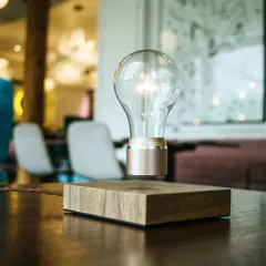 The FLYTE Buckminster levitating light bulb is a piece of minimalist art that floats and glows. Powered wirelessly through the air, it uses an energy-efficient LED and is set on a sustainable walnut wood base, making it a unique decor item or a memorable gift.