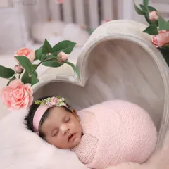 Pretty in pink. This baby girl is nestled in a heart-shaped bowl, surrounded by soft pink fur and delicate pink roses for a romantic and classic floral portrait.
