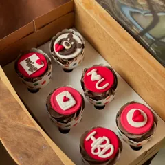 A closer look at the custom love-themed cupcakes. The fondant toppers include messages like "I heart U", "Mine", and a cute teddy bear.
