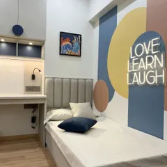 This shared kids' bedroom uses bold color blocking and a "Love Learn Laugh" neon sign to create a vibrant, inspiring atmosphere. A single bed is set against the mural, with a shared study area nearby.
