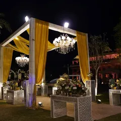The entrance structure for the 'Golden Grandeur' theme, featuring a modern white frame with golden drapes and a hanging chandelier, setting a tone of contemporary luxury.