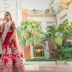 A breathtaking full-length shot of a bride in her red lehenga, standing in the courtyard of a European-style luxury hotel.