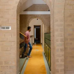 An arched hallway in the Audumbara house, with exposed brick walls and a yellow Jaisalmer stone floor runner, guiding the way through the home.