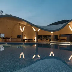 This is the Aqua Pool & Spa, a modern cave-like structure designed to celebrate the surrounding hills. The evening view highlights the custom lighting which reflects in the water, creating a tranquil and immersive atmosphere that blends architecture with the natural landscape.