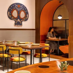 In Tres Amigos, we created intimate arched booths for a cozy dining experience. The warm orange interior of the booth contrasts with the neutral walls, while a custom-designed skull rug adds a touch of modern Mexican artistry, making it a popular photo spot for guests.