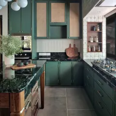 A wider view of this green kitchen, showing how the different elements work in harmony. The open spice nook, the warm lighting, and the patterned ceiling all contribute to a space that is as functional for cooking as it is inviting for gathering.