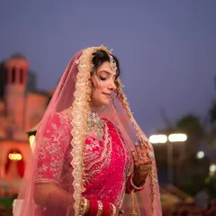 A beautiful North Indian bride in a pink lehenga, her veil framing her face perfectly against the evening sky.