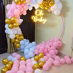 A modern baby shower setup with a pink, blue, white, and gold balloon ring. The 'Oh Baby' neon sign adds a trendy touch to the celebration.