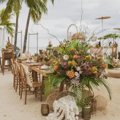 A stunning, oversized floral arrangement featuring exotic tropical flowers and palm leaves, serving as a dramatic centerpiece for the beach event.